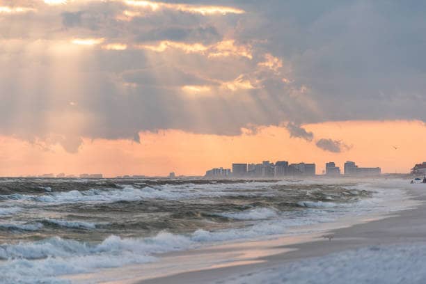 Dramatic magical pastel light sunset with sun rays in Santa Rosa Beach, Florida with Pensacola coastline coast cityscape skyline in panhandle and ocean gulf mexico waves